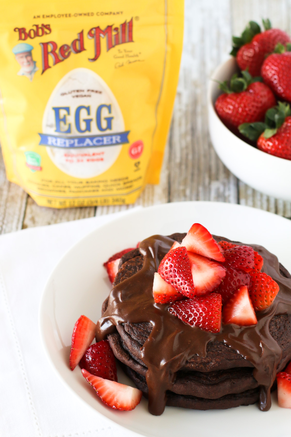 Gluten Free Vegan Double Chocolate Pancakes, featuring Bob’s Red Mill egg replacer. Fluffy chocolate pancakes, covered in a simple chocolate sauce and fresh strawberries. Quite the decadent breakfast!